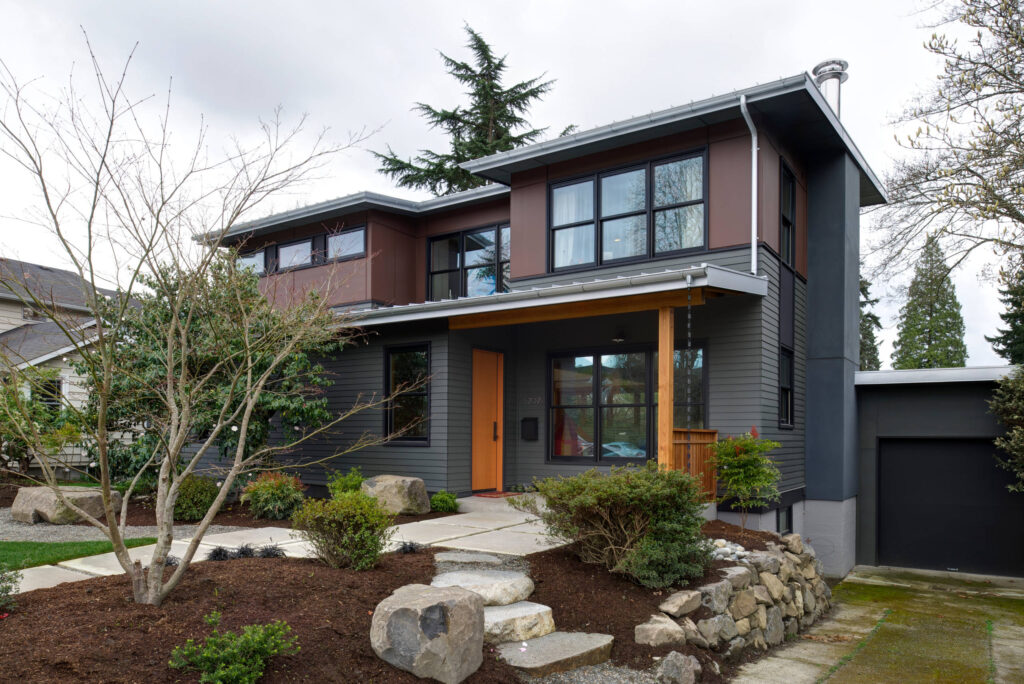 Modern two-story home with gray siding, large black-framed windows, and a natural wood front door.