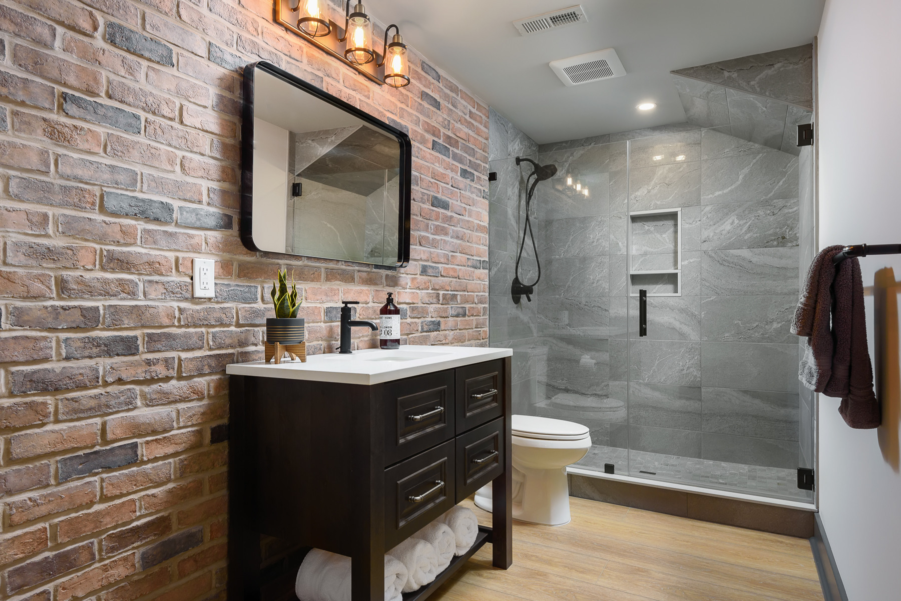 Industrial-style bathroom with brick accent wall, gray tile shower, and dark wood vanity.
