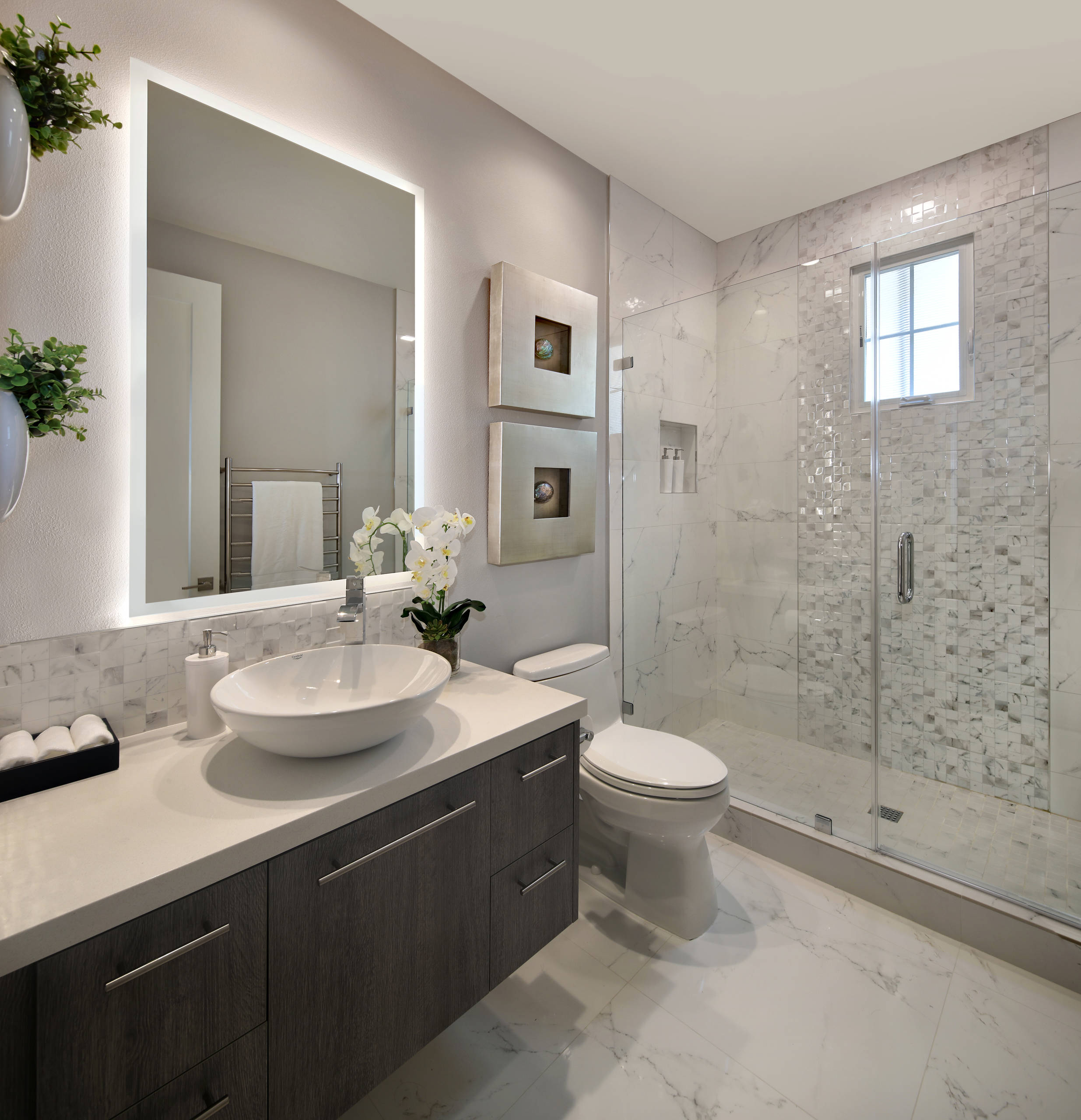 Contemporary bathroom with lighted vanity mirror, vessel sink, and glass-enclosed shower.