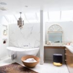 Luxurious bathroom with skylights, freestanding white tub, marble walls, and Moroccan-inspired decor.