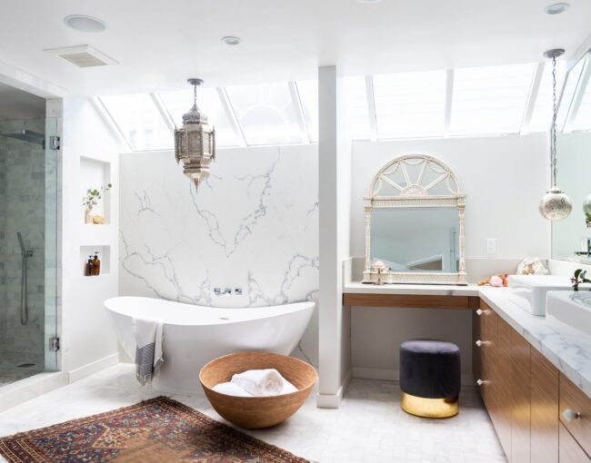 Luxurious bathroom with skylights, freestanding white tub, marble walls, and Moroccan-inspired decor.