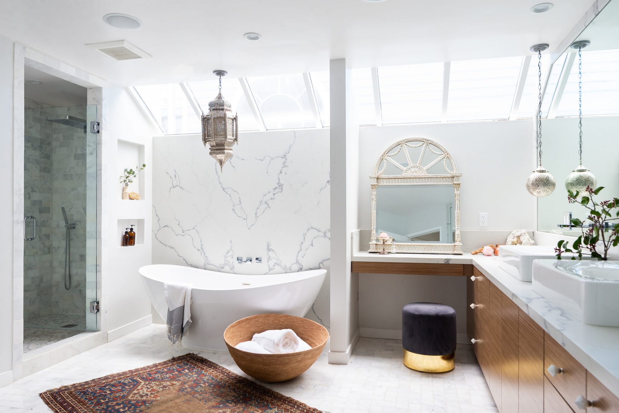 Luxurious bathroom with skylights, freestanding white tub, marble walls, and Moroccan-inspired decor.