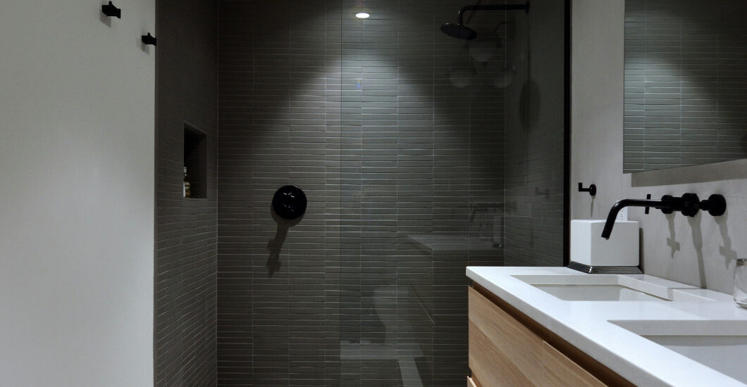 Modern bathroom with glass-enclosed shower, wood vanity, and black fixtures.
