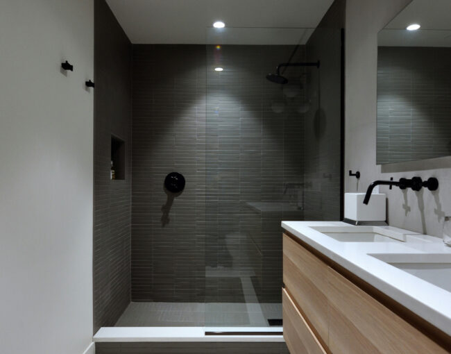 Modern bathroom with glass-enclosed shower, wood vanity, and black fixtures.