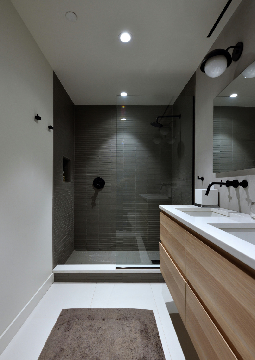 Modern bathroom with glass-enclosed shower, wood vanity, and black fixtures.