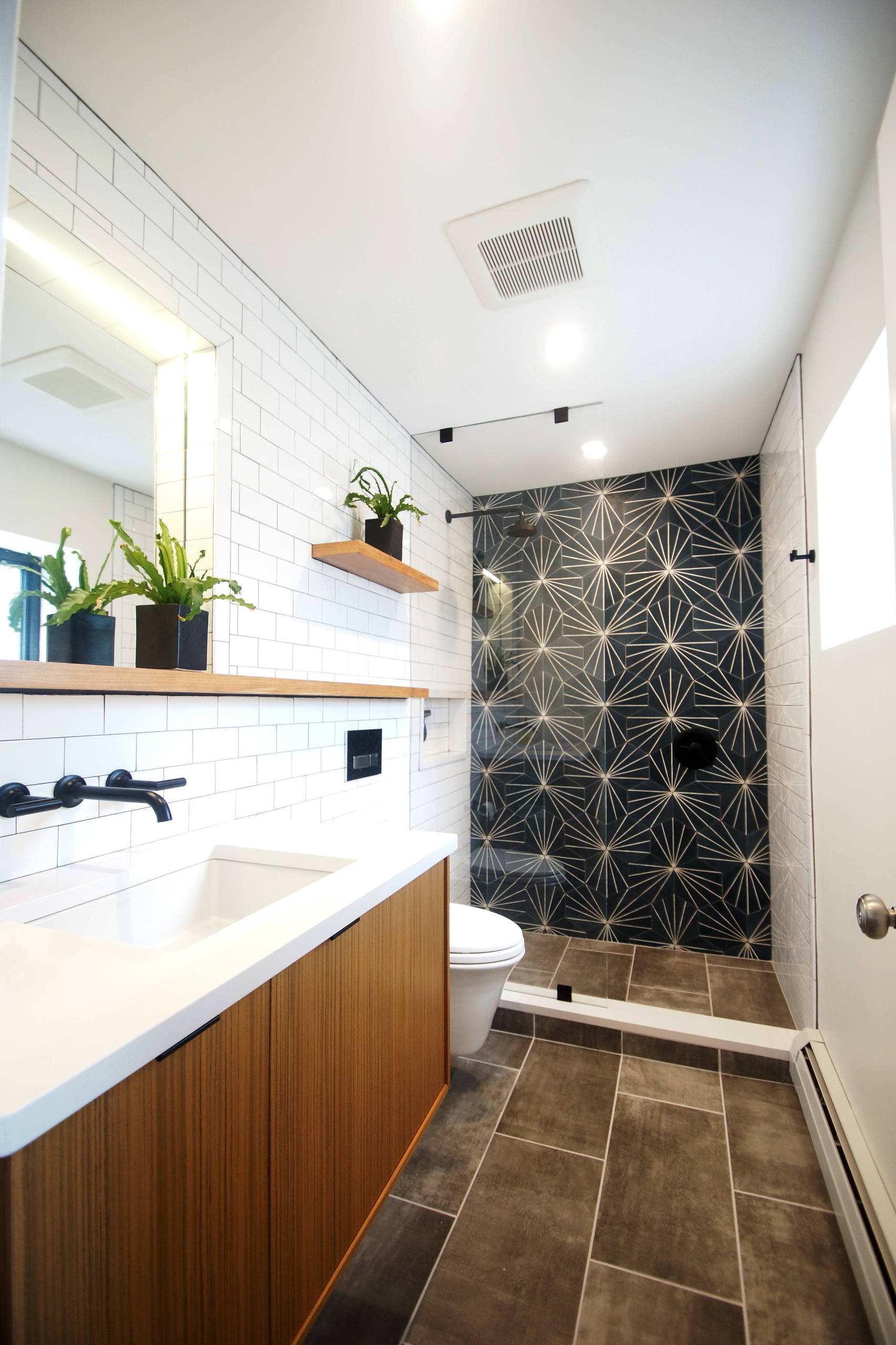 Modern bathroom with geometric shower tile, wood vanity, and white subway tile walls.