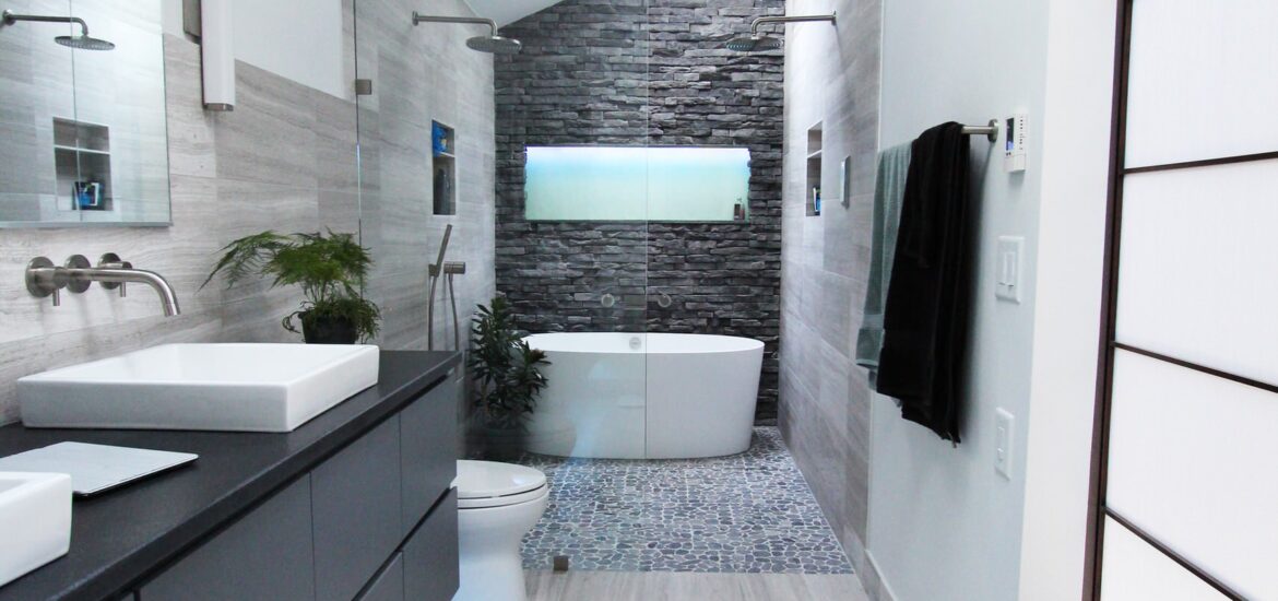 Modern bathroom with freestanding tub, stone accent wall, and sleek gray vanity.