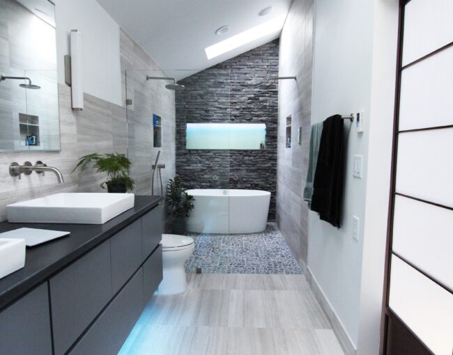 Modern bathroom with freestanding tub, stone accent wall, and sleek gray vanity.