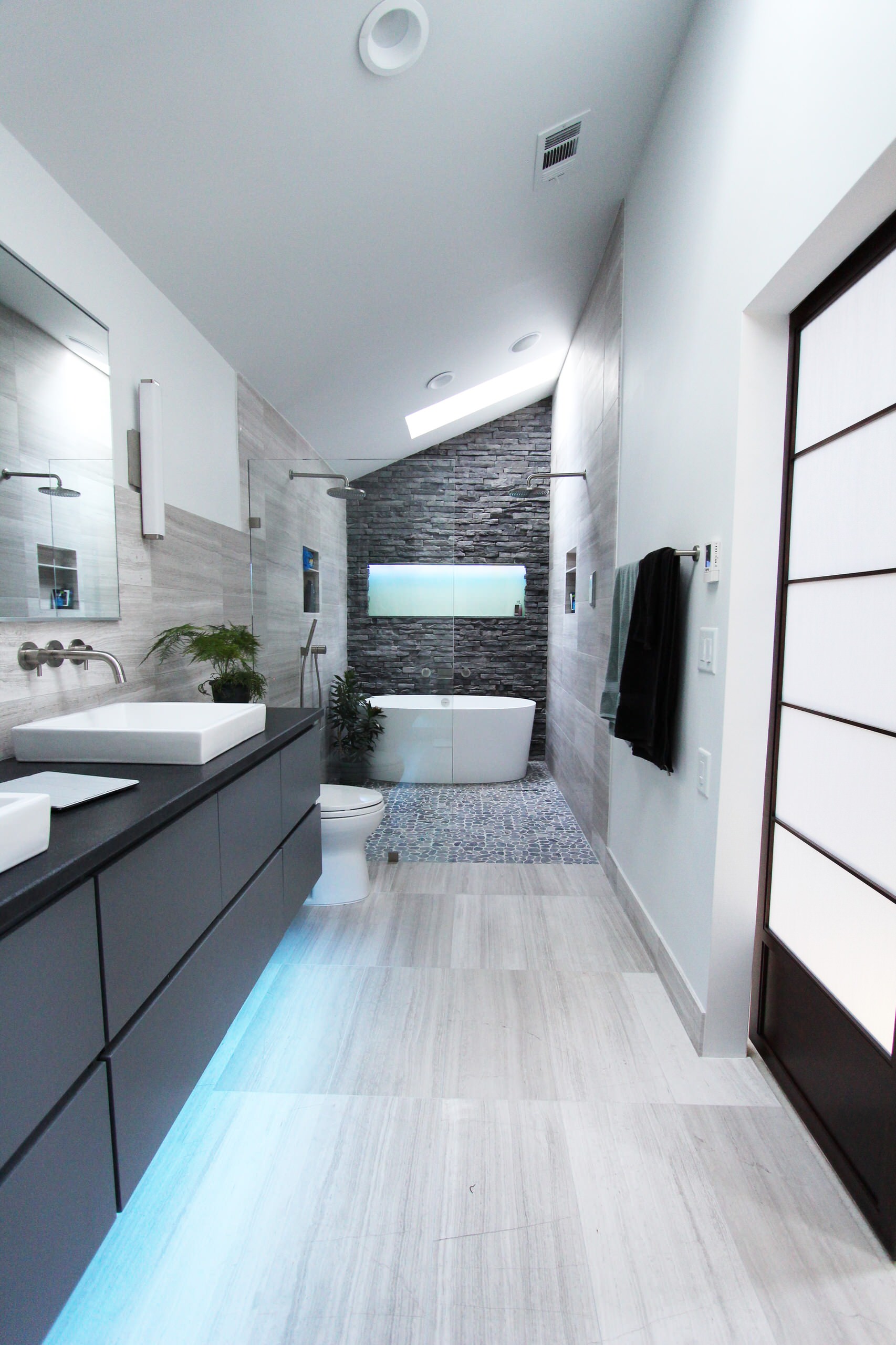 Modern bathroom with freestanding tub, stone accent wall, and sleek gray vanity.