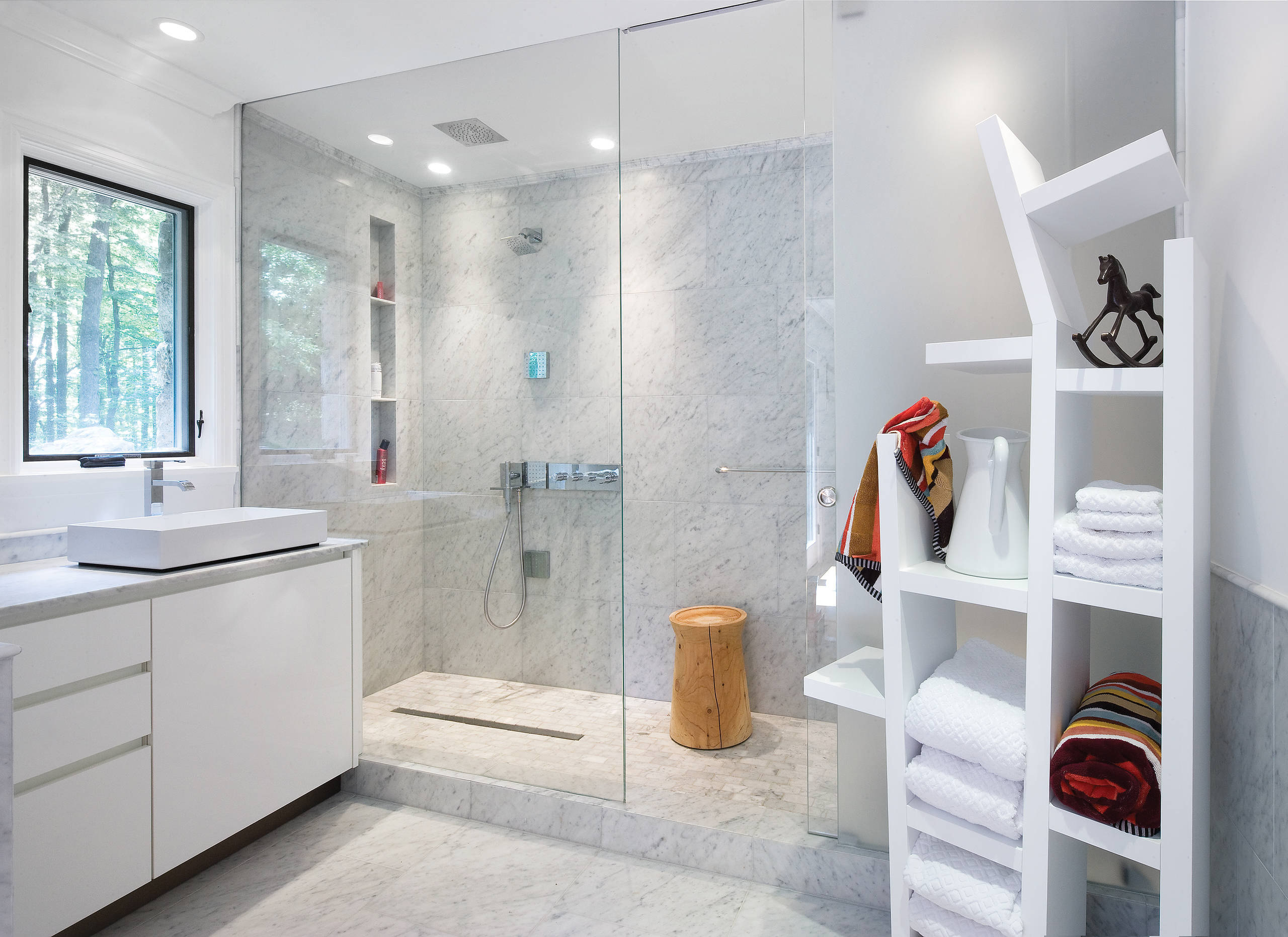 Modern bathroom with marble walls and floors, glass shower enclosure, and open shelving.