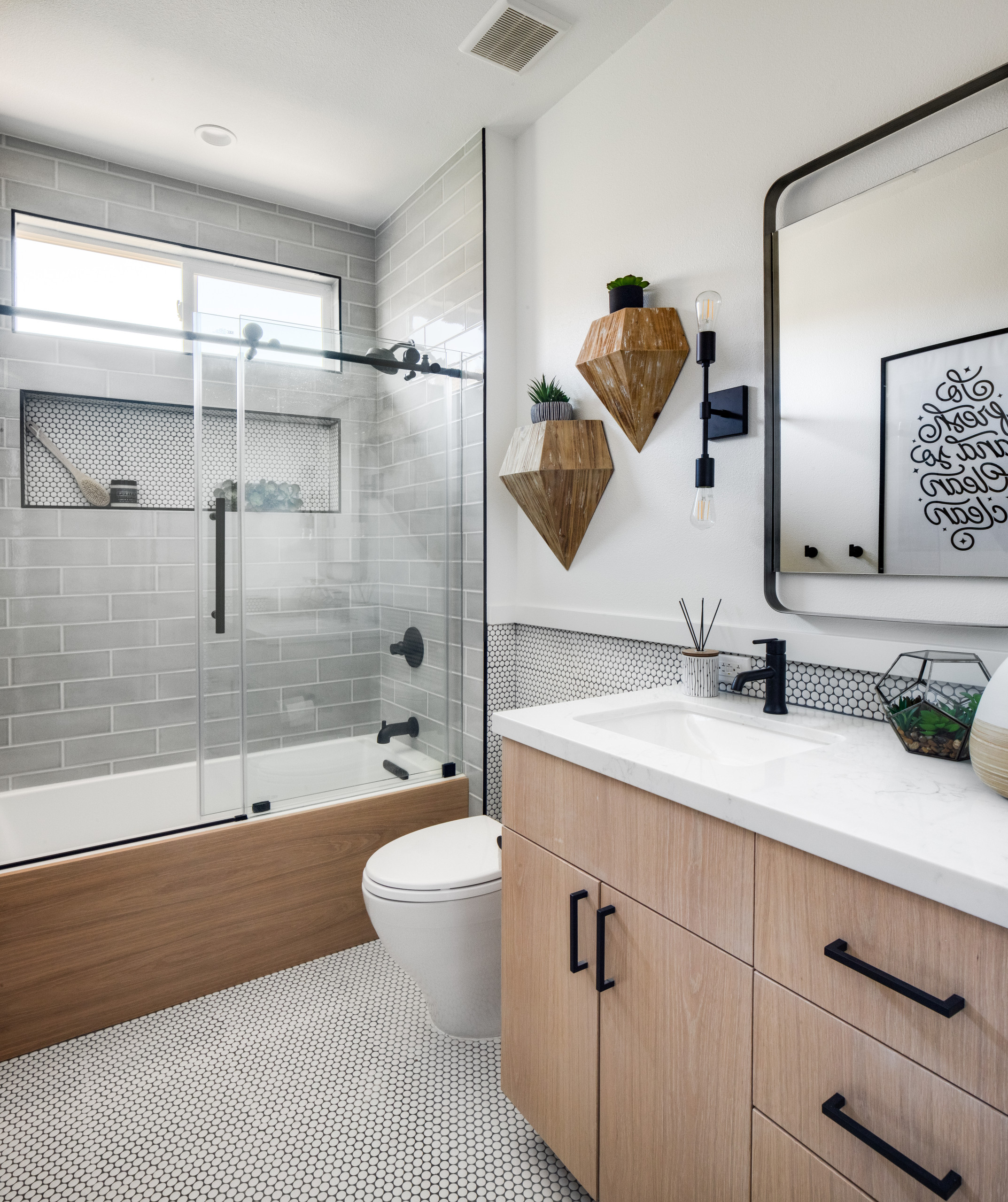 Modern bathroom with wood vanity, gray subway tile shower, and black fixtures.
