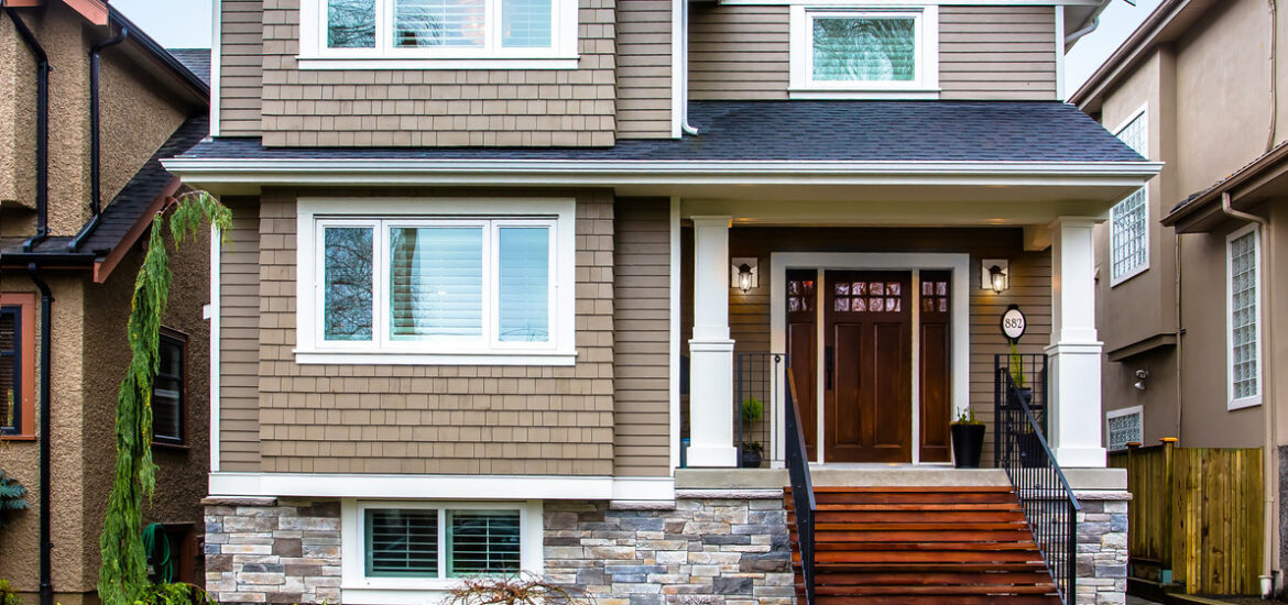 Two-story suburban home with brown shingle siding, stone accents, and a front porch entrance.