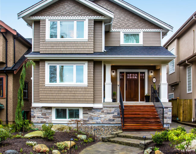 Two-story suburban home with brown shingle siding, stone accents, and a front porch entrance.