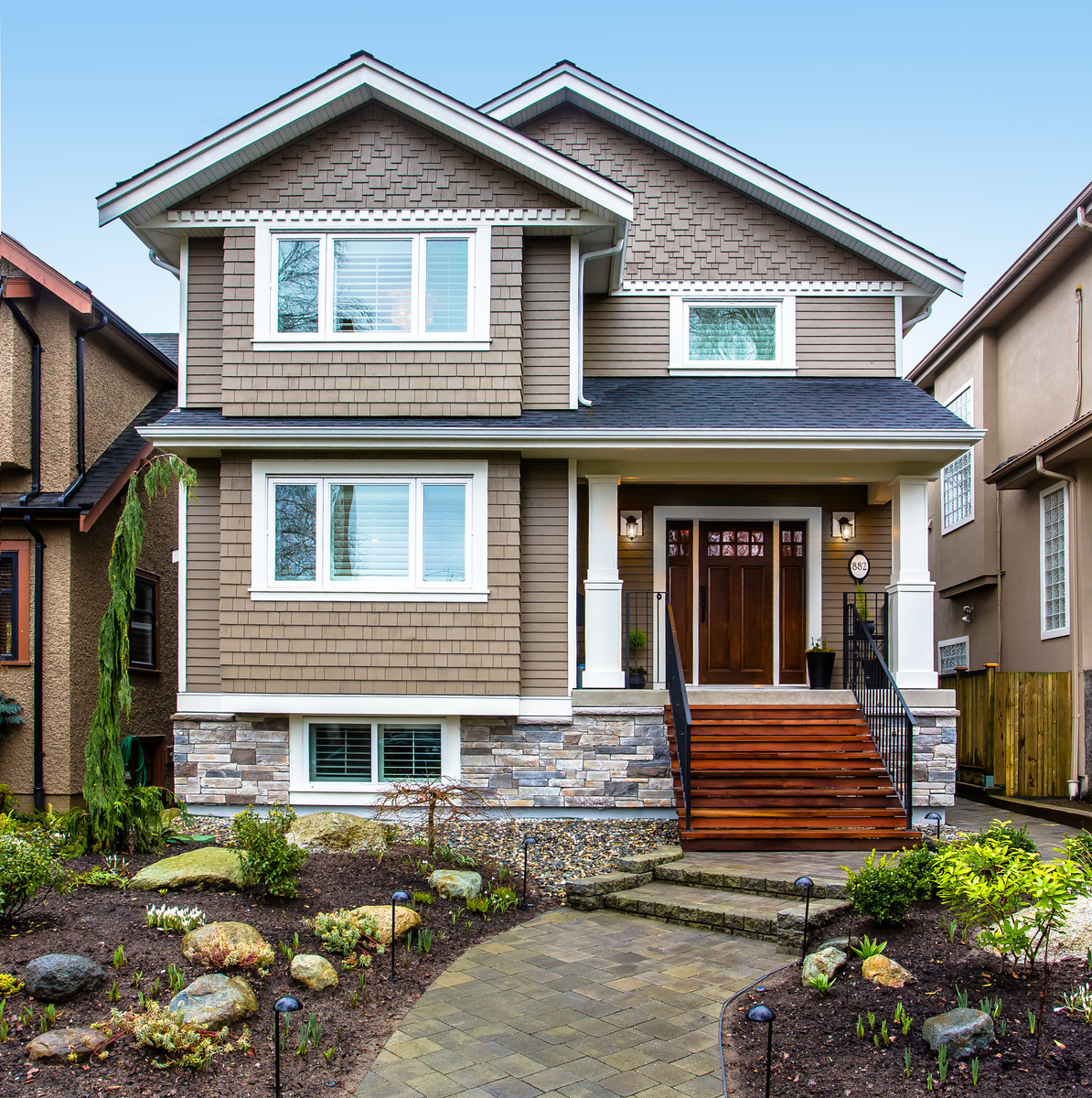 Two-story suburban home with brown shingle siding, stone accents, and a front porch entrance.