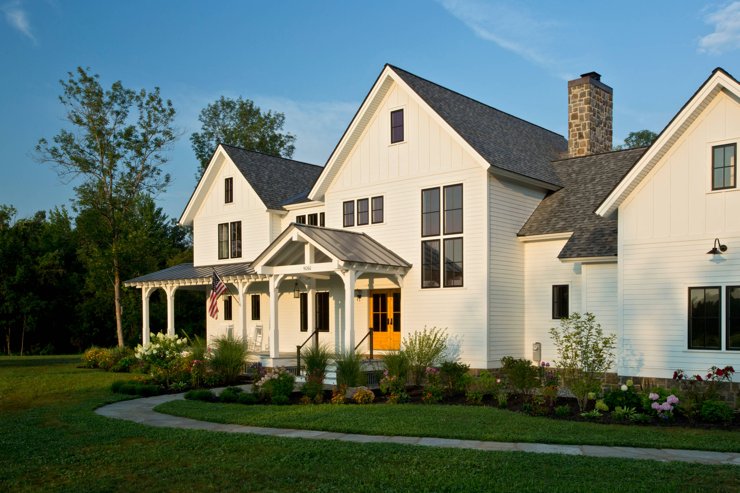 Modern white farmhouse with black windows, front porch, and landscaped garden