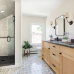 Bright bathroom with wood double vanity, glass shower, and patterned tile floor.