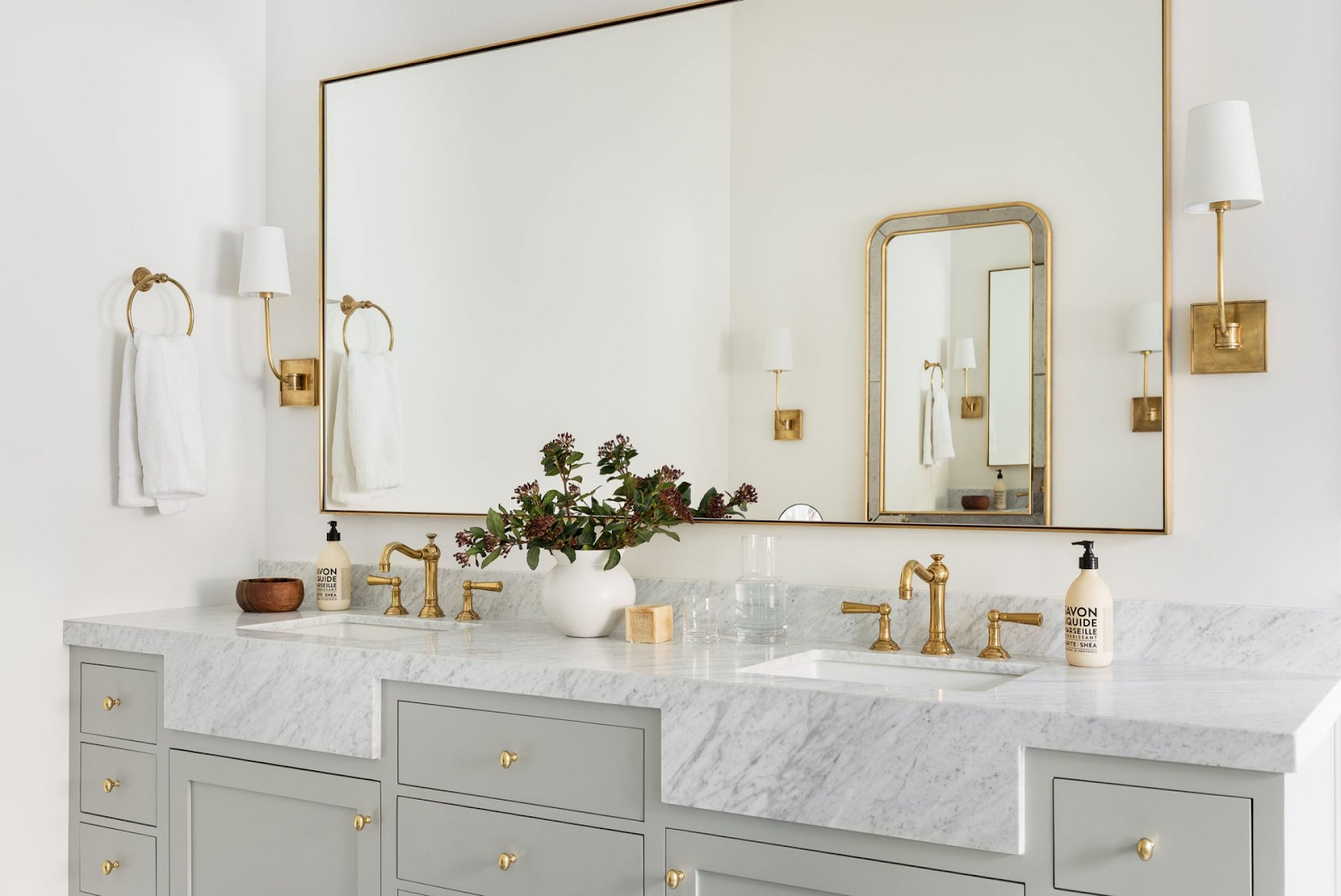 Elegant double bathroom vanity with light gray cabinets, marble countertop, gold fixtures, and a large wall mirror.