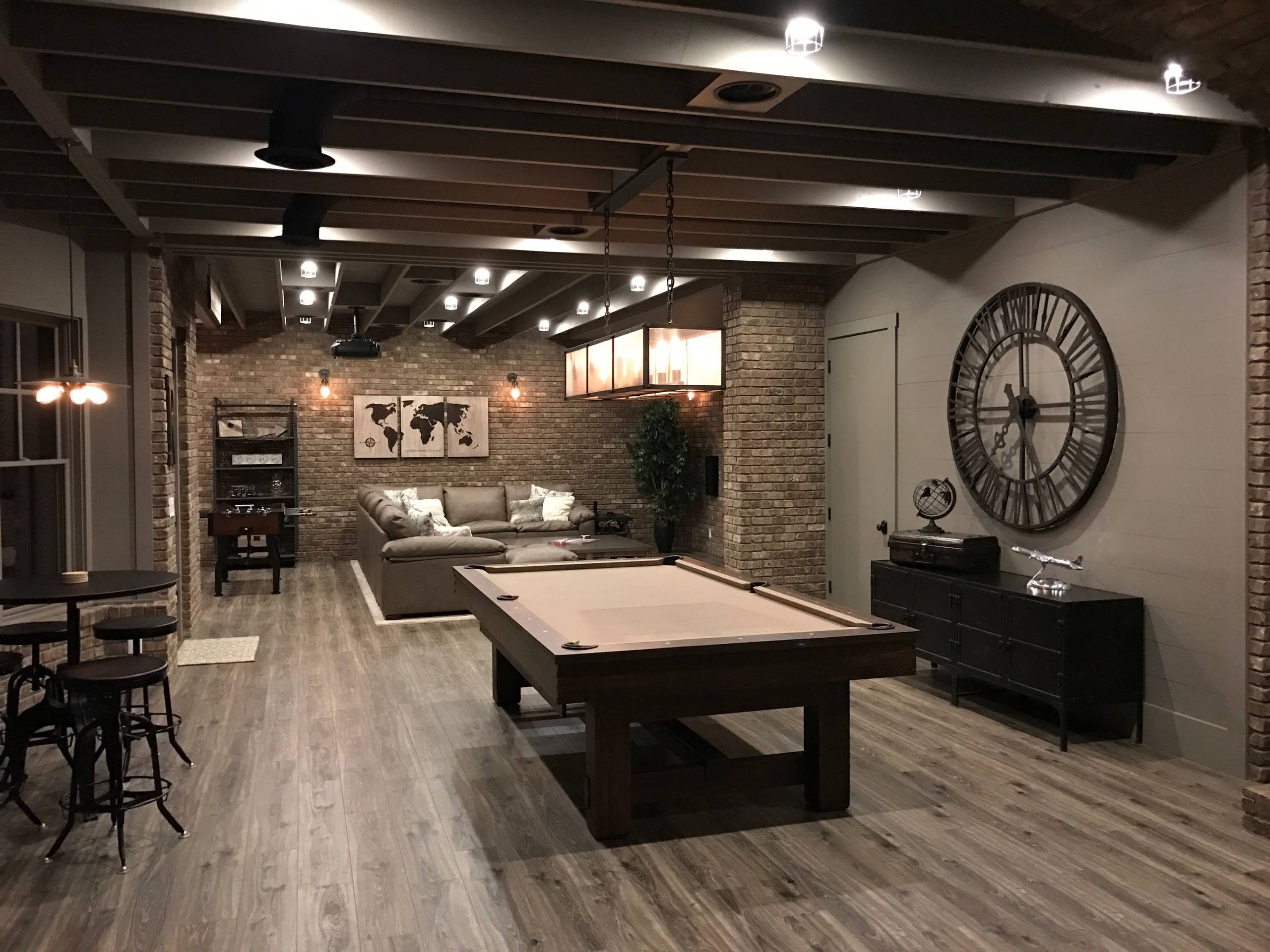 Industrial-style basement with exposed brick walls, wood flooring, and a pool table