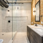 Industrial bathroom with marble tile shower, exposed brick wall, and double vanity.