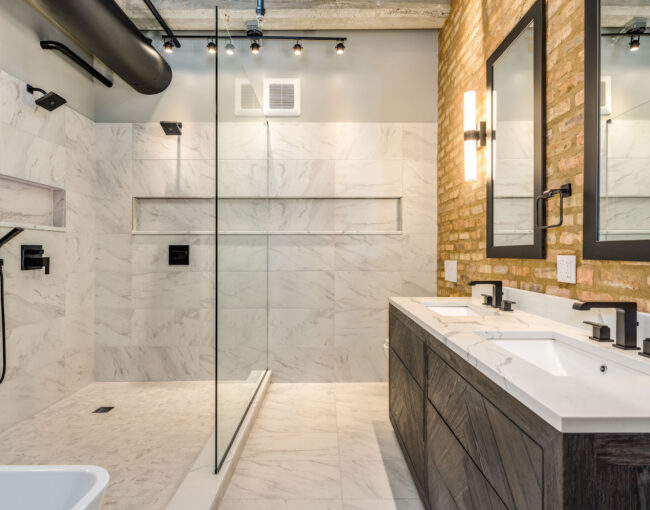 Industrial bathroom with marble tile shower, exposed brick wall, and double vanity.