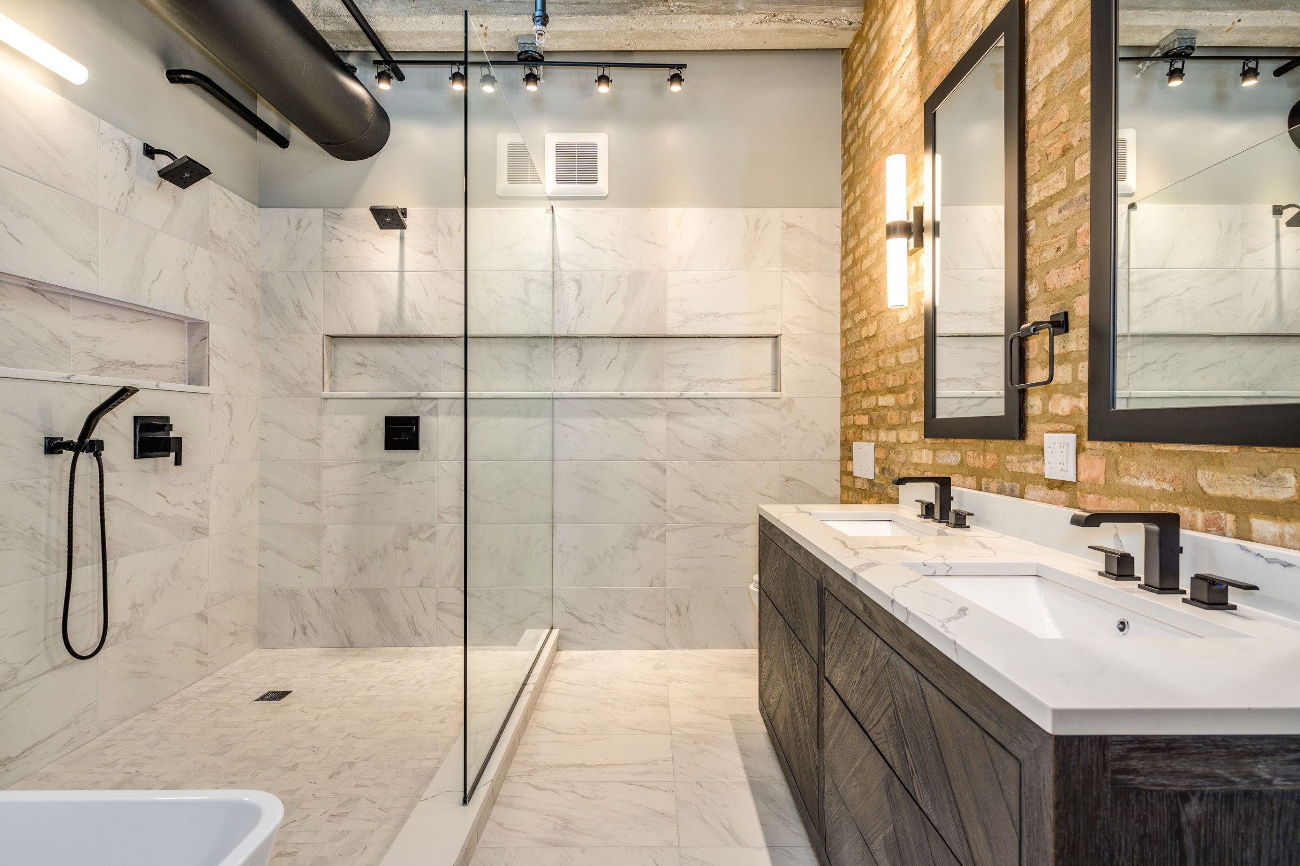 Industrial bathroom with marble tile shower, exposed brick wall, and double vanity.