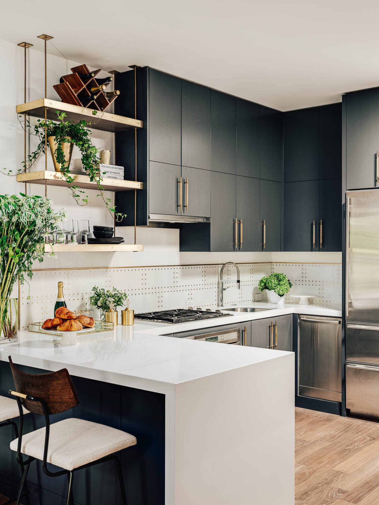 Modern kitchen with dark cabinetry, open gold shelving, and a white quartz peninsula.