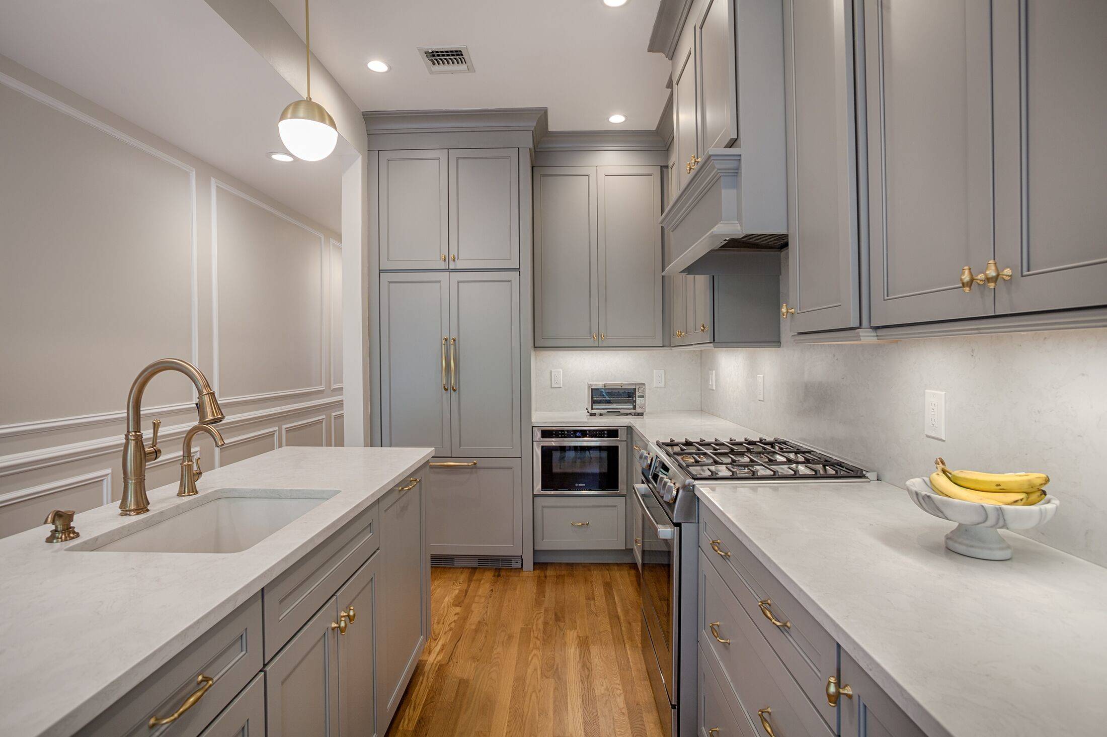 Narrow galley kitchen with gray cabinetry, brass hardware, and white quartz countertops.