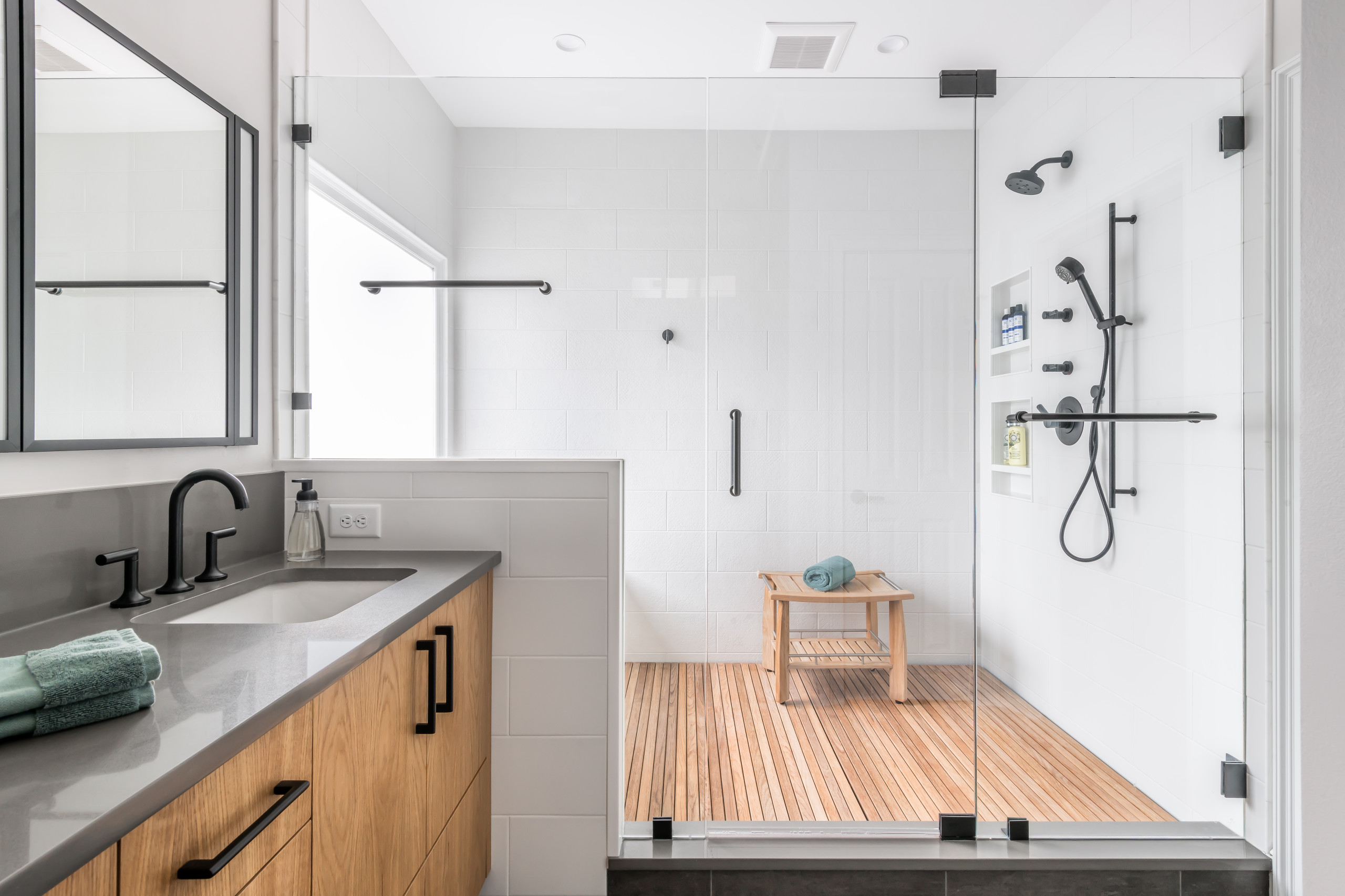 Contemporary bathroom with glass-enclosed shower featuring teak floor and black fixtures.