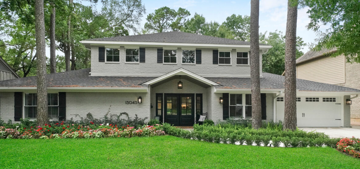 Two-story remodeled home with light brick exterior, black shutters, and landscaped front yard.