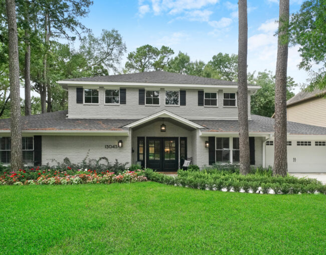 Two-story remodeled home with light brick exterior, black shutters, and landscaped front yard.