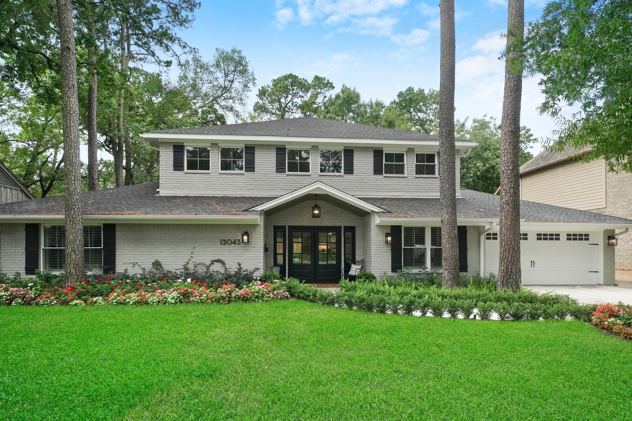 Two-story remodeled home with light brick exterior, black shutters, and landscaped front yard.