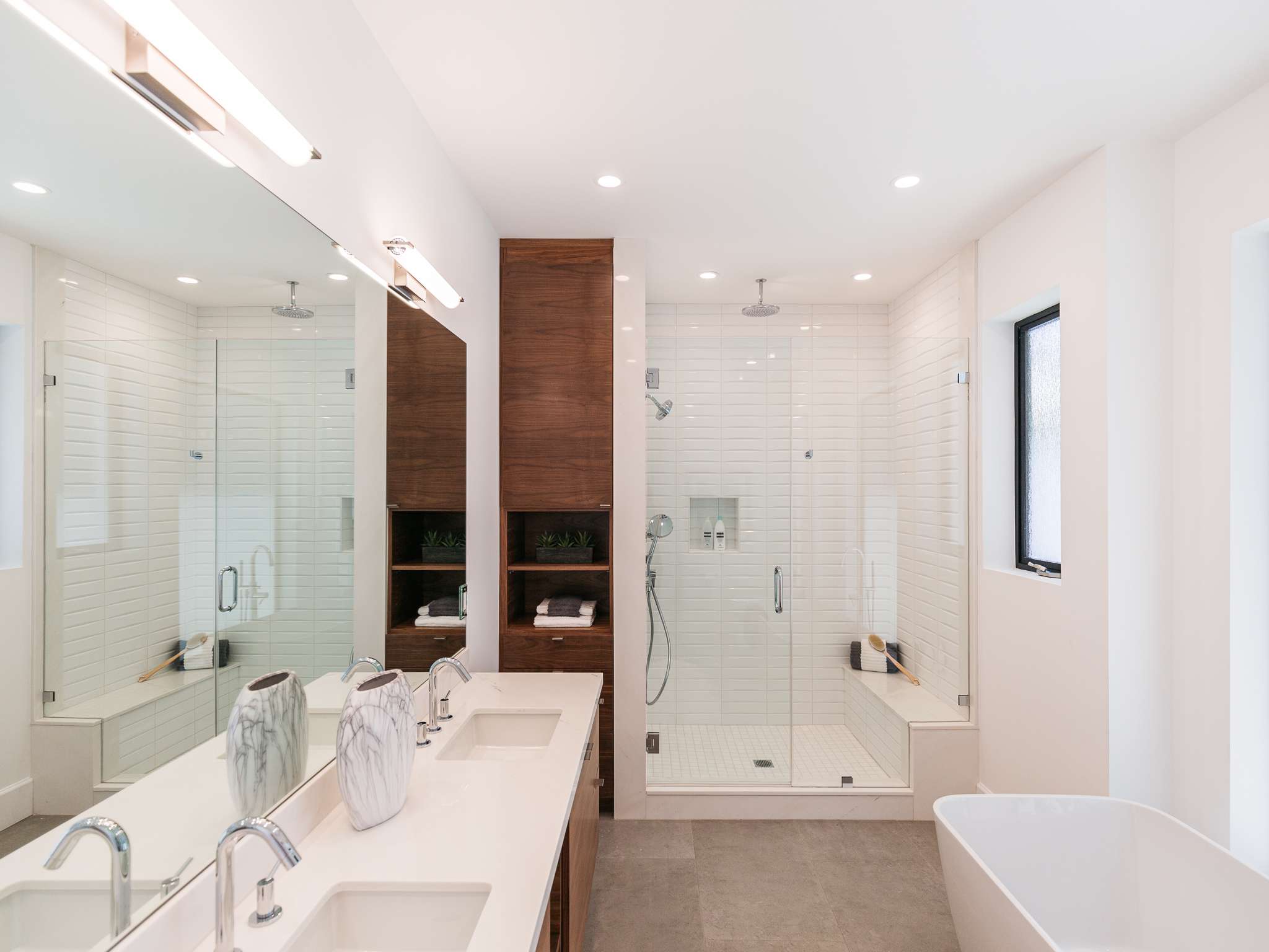 Modern bathroom with double shower, wooden cabinetry, and freestanding bathtub.