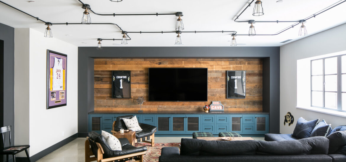 Modern basement media room with large TV, wood accent wall, and sports memorabilia.