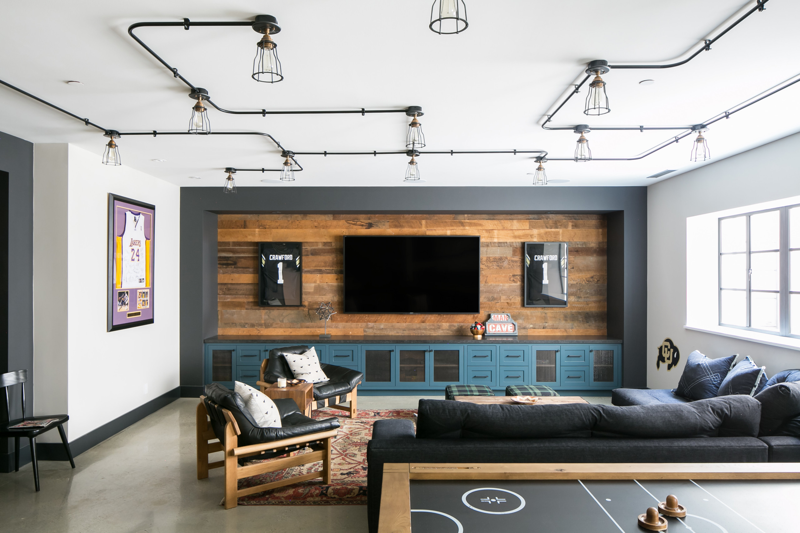 Modern basement media room with large TV, wood accent wall, and sports memorabilia.