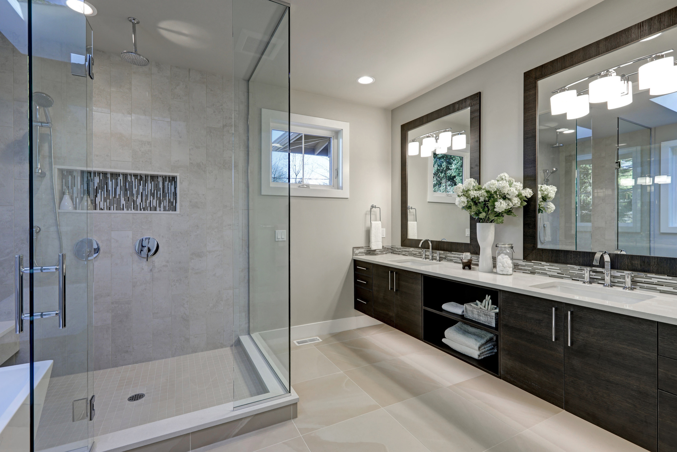 Modern bathroom with glass-enclosed shower, double vanity, and large framed mirrors.