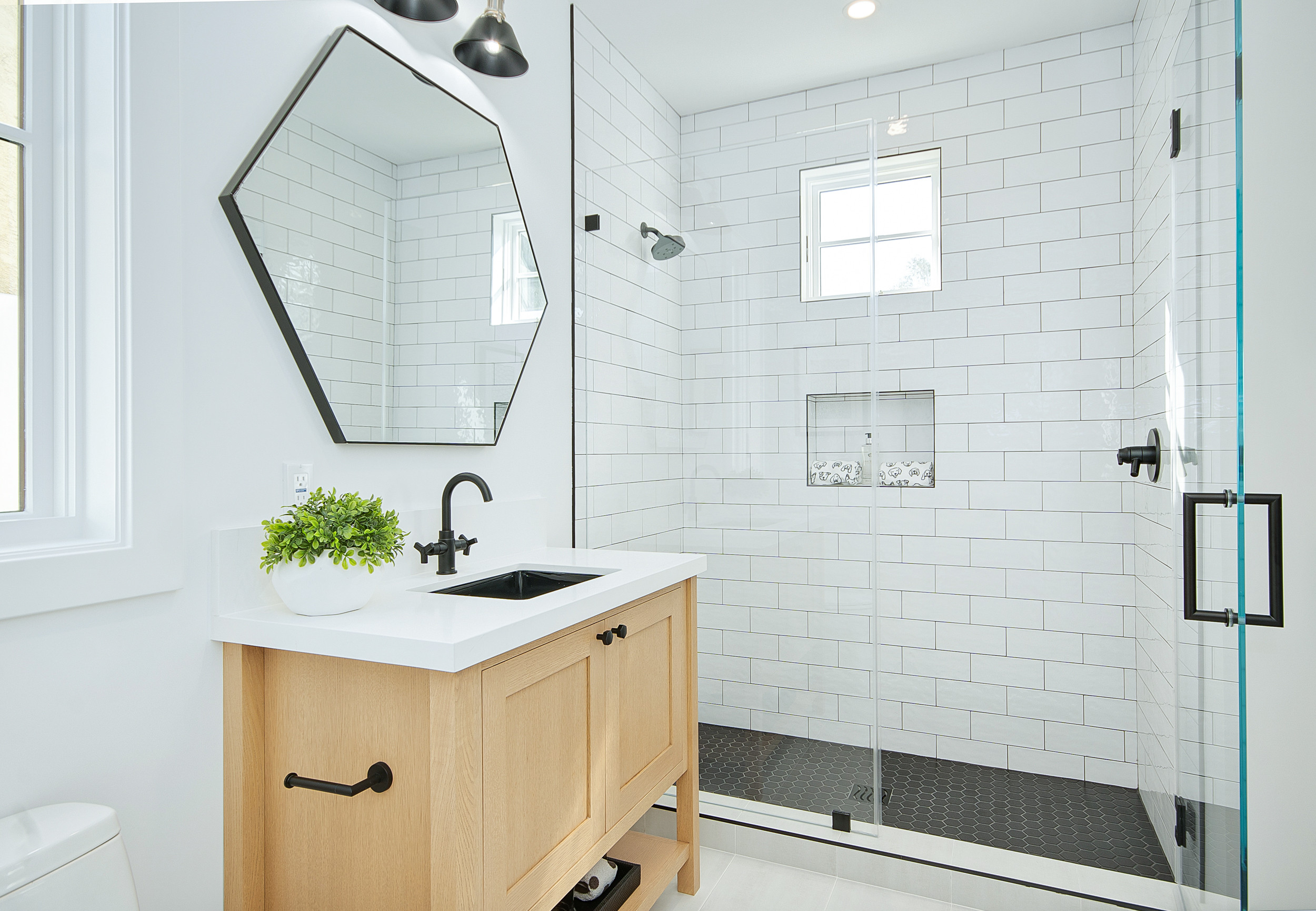 Modern bathroom with wood vanity, hexagonal mirror, and glass-enclosed shower.