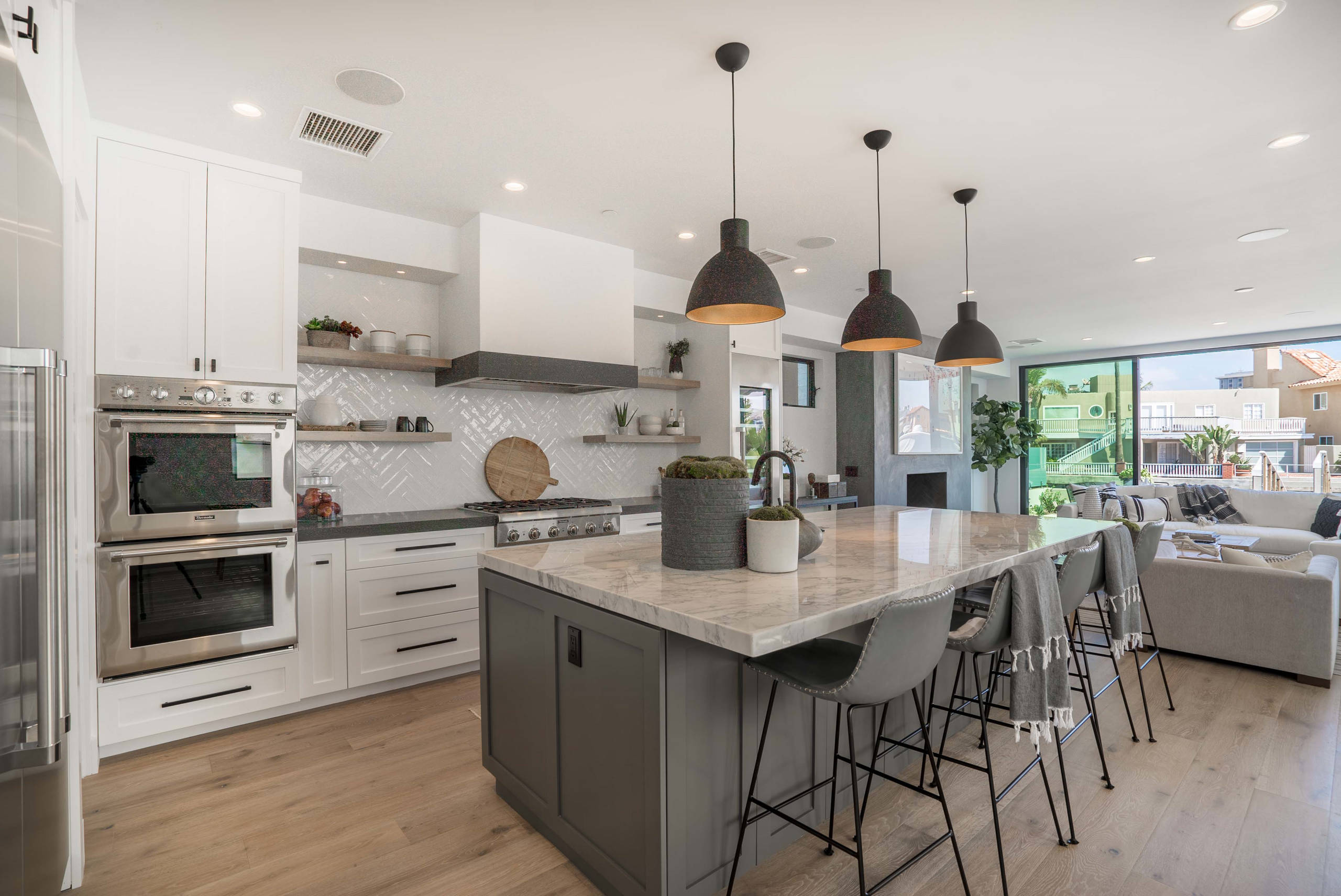 Modern open-concept kitchen with marble island, pendant lights, and indoor-outdoor living space.