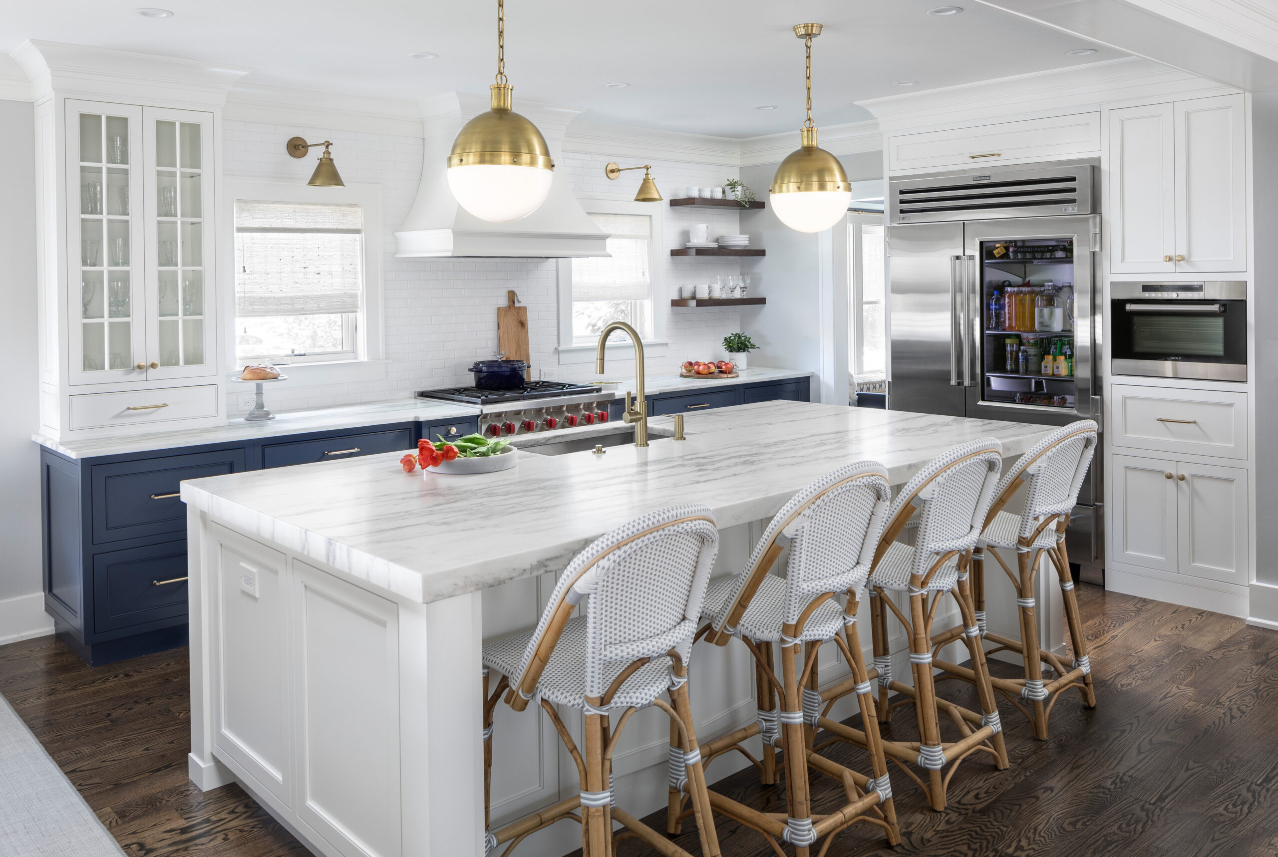 Bright coastal-inspired kitchen with white and navy cabinets, marble island countertop, and brass fixtures.