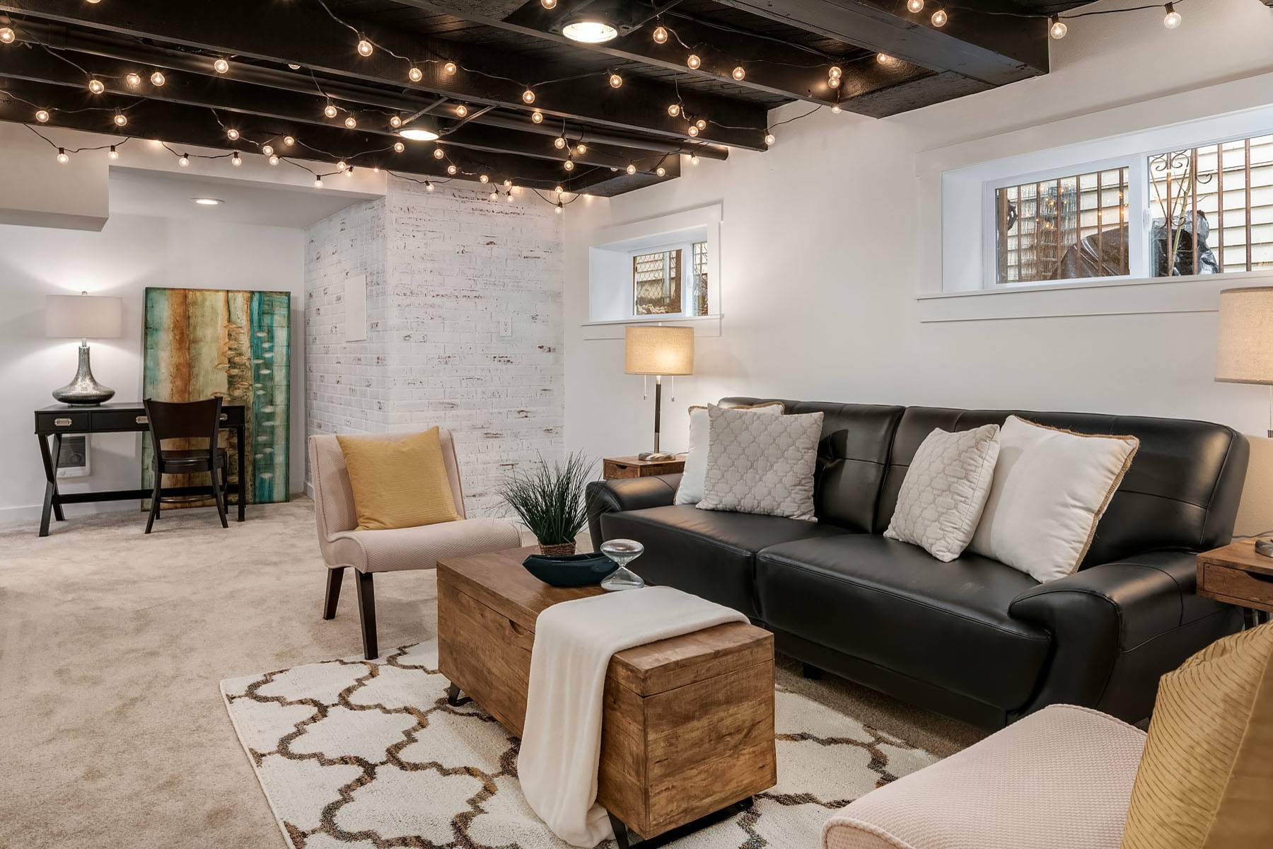Cozy finished basement with string lights, black sofa, and rustic decor.