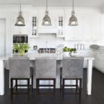 Bright white kitchen with marble island, stainless steel accents, and gray upholstered bar stools.