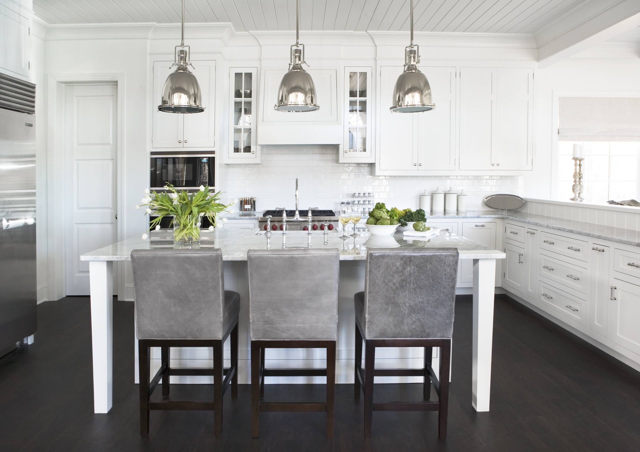 Bright white kitchen with marble island, stainless steel accents, and gray upholstered bar stools.