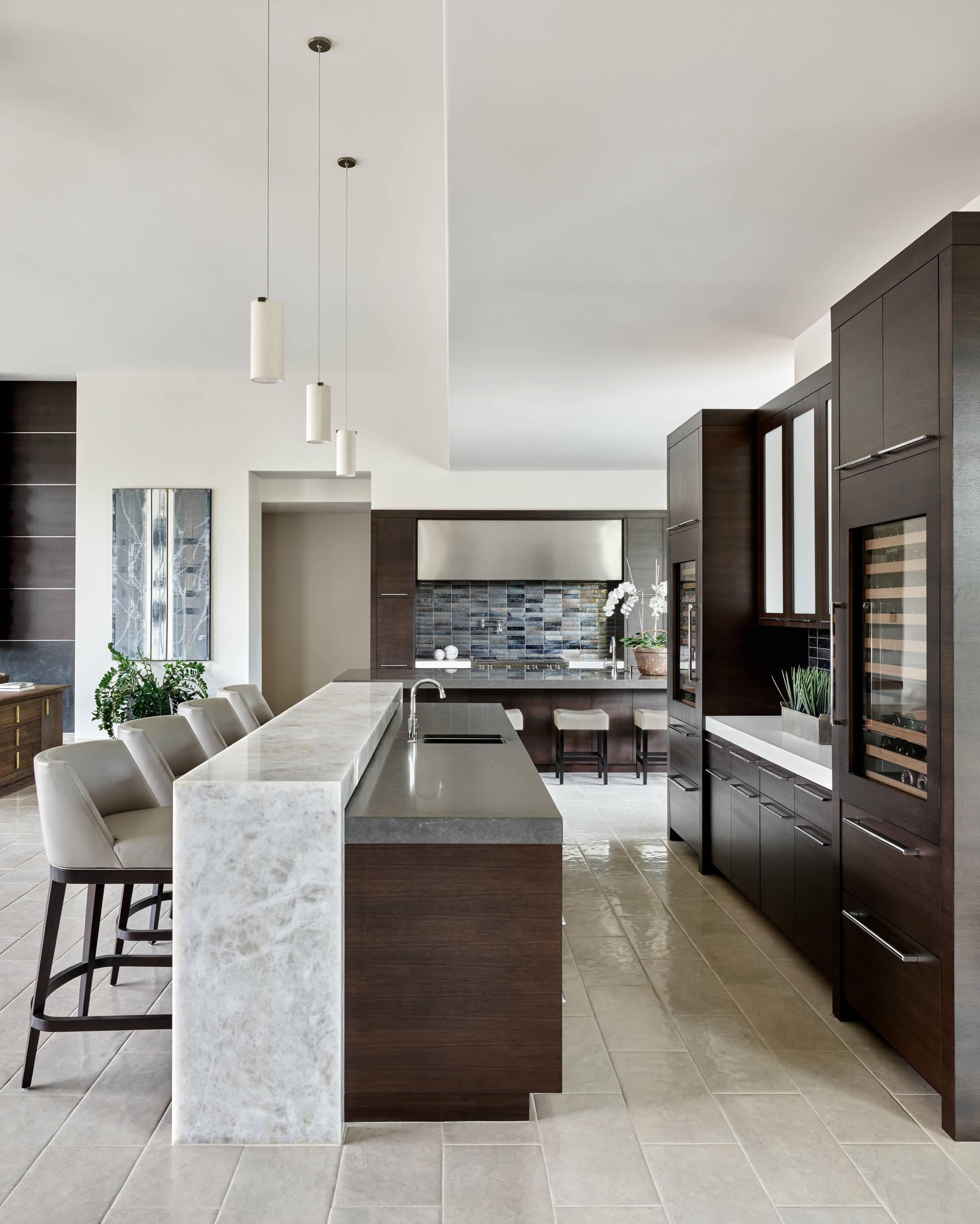 Modern luxury kitchen with dark wood cabinetry, sleek countertops, and marble waterfall bar.