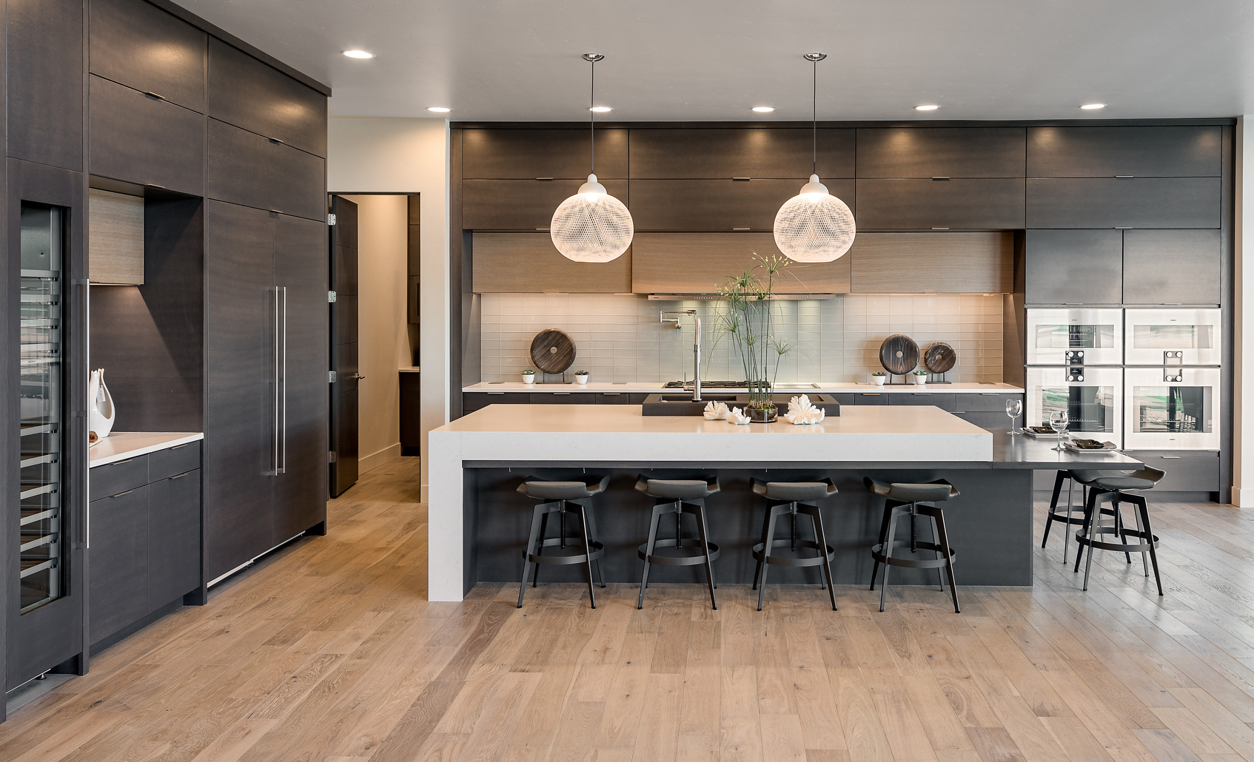 Modern kitchen with dark wood cabinetry, large white waterfall island, and minimalist bar stools.