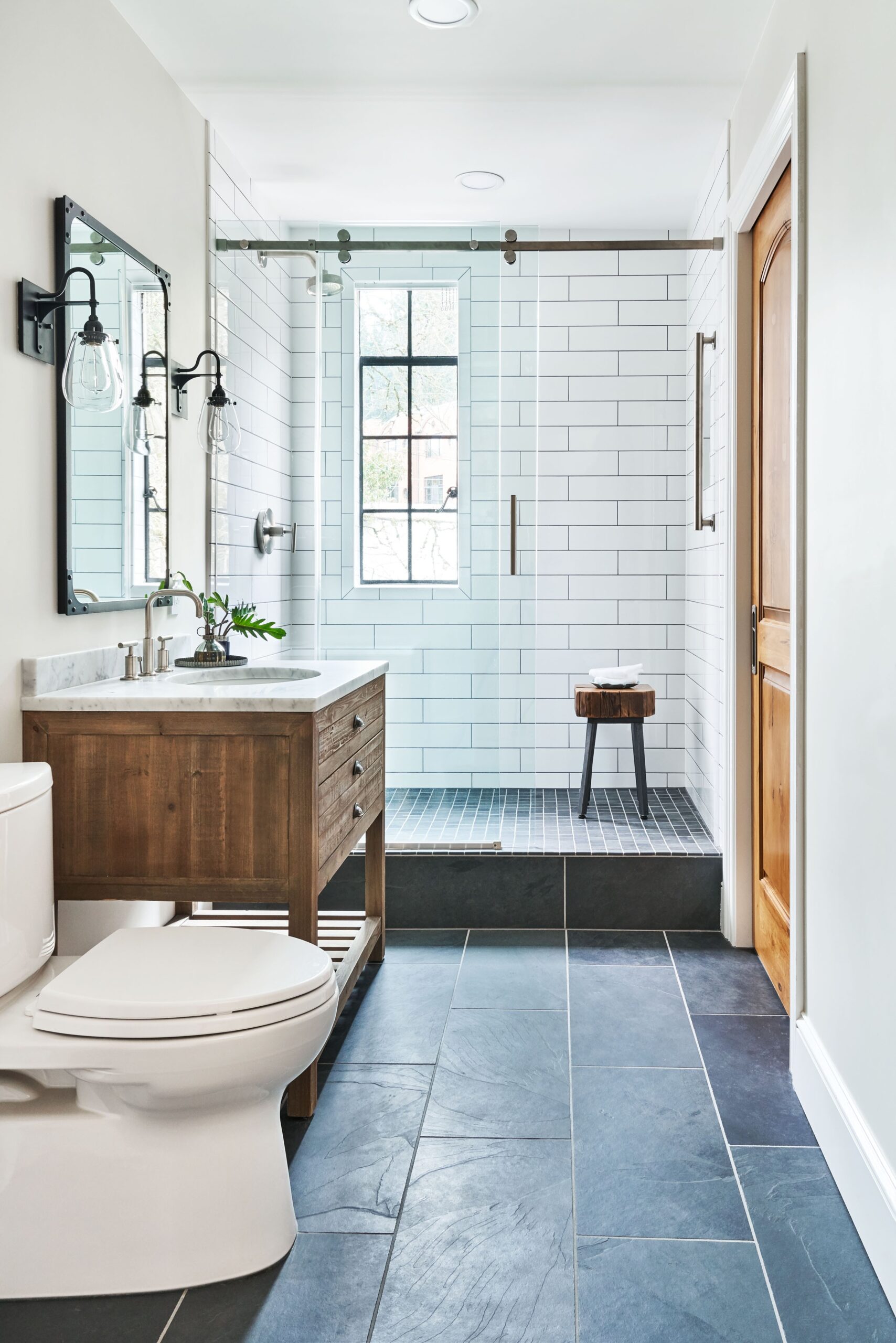 Modern bathroom with wood vanity, glass-enclosed shower, and slate tile flooring.