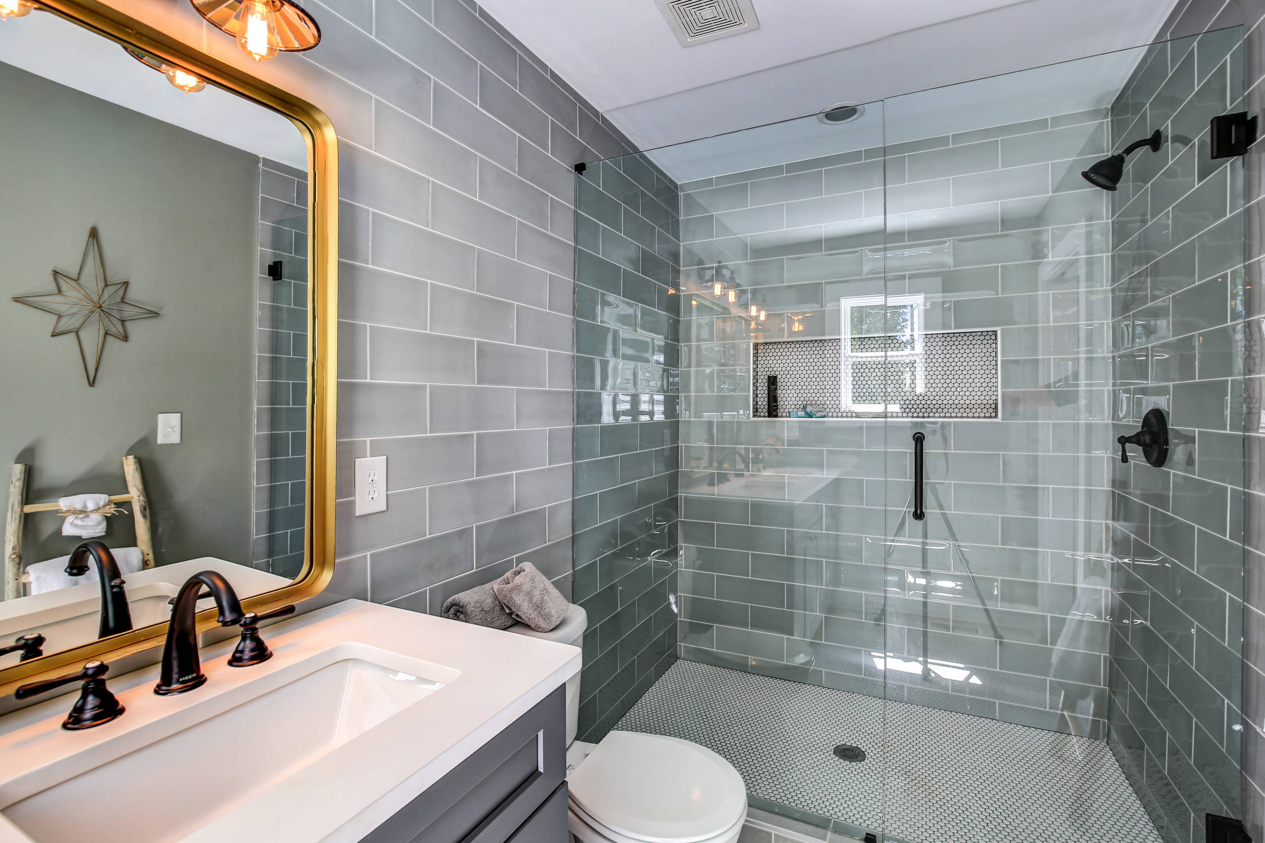 Modern bathroom with glass-enclosed shower and gray subway tile walls.