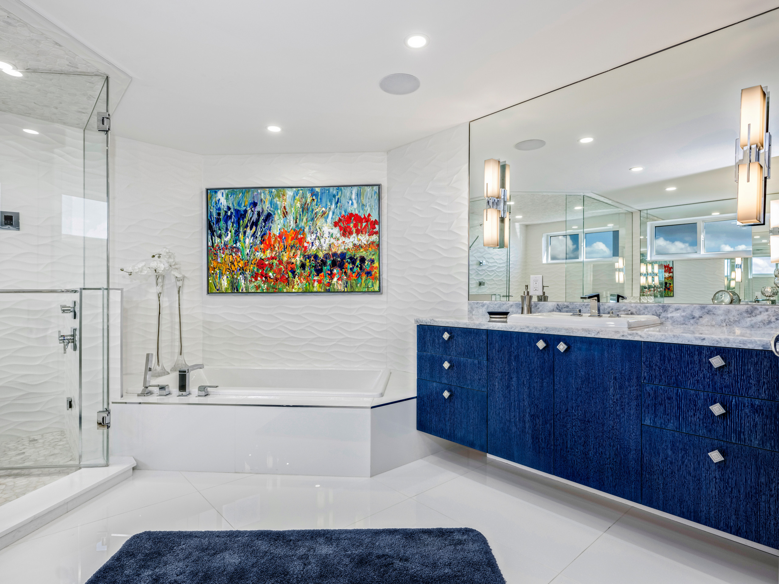 Luxurious modern bathroom with blue vanity, glass shower, and vibrant wall art.