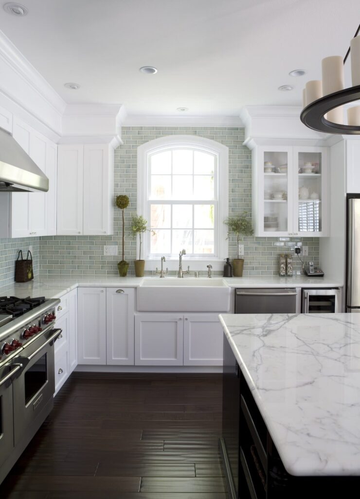 Bright kitchen with white cabinetry, marble countertops, and green subway tile backsplash.
