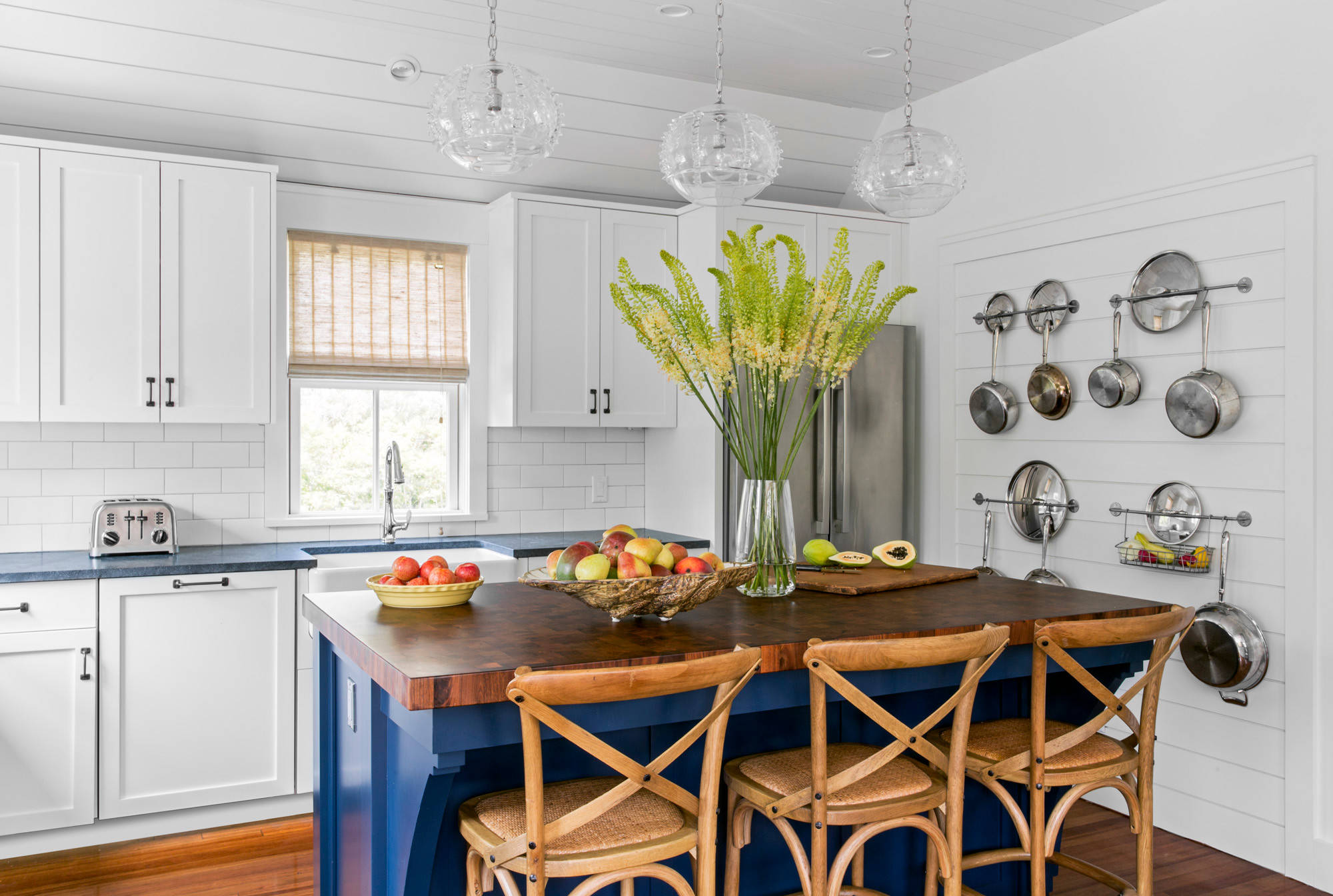 Coastal kitchen with navy blue island, white cabinetry, and wall-mounted stainless steel cookware.