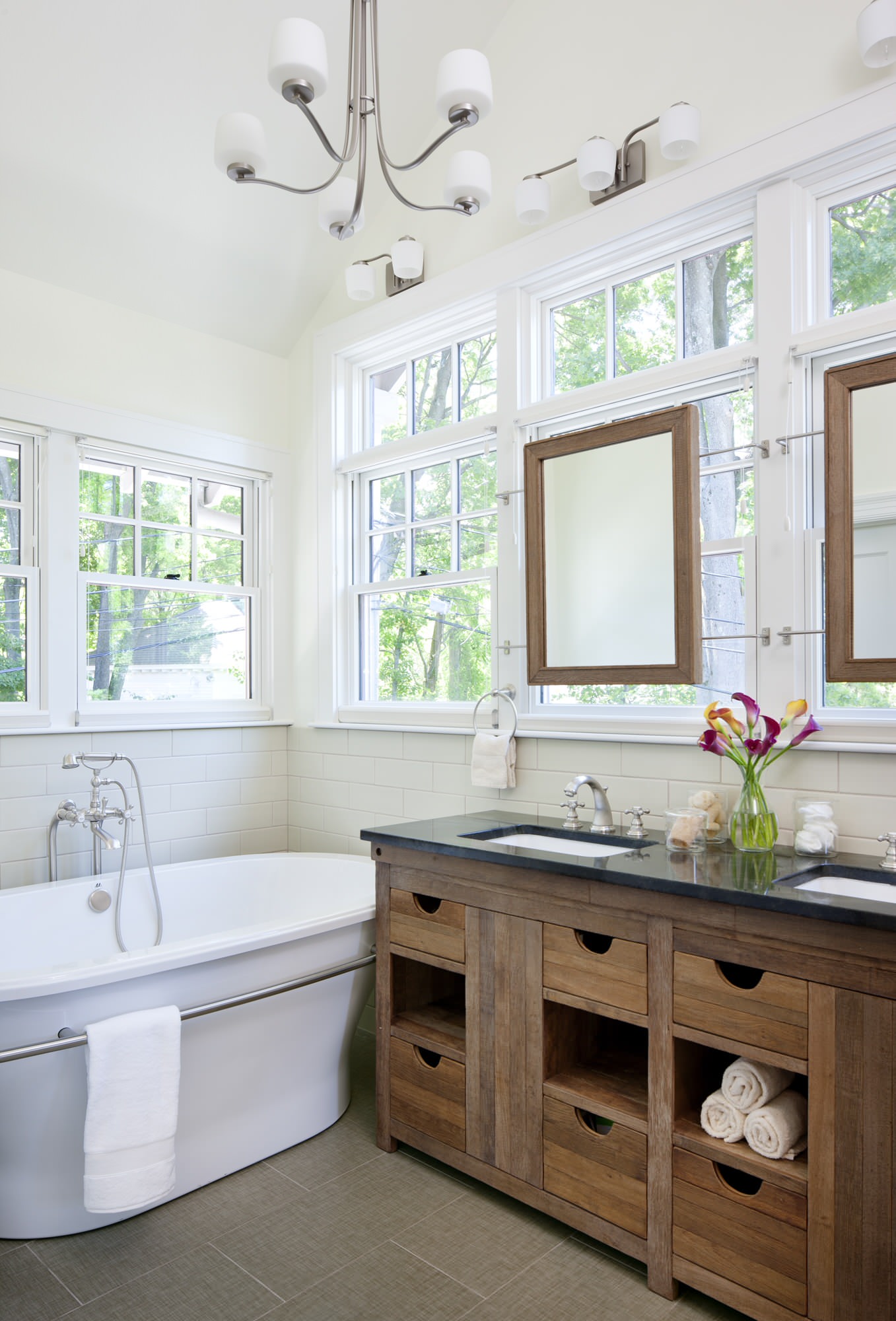 Bright bathroom with freestanding tub, wood vanity, and large windows.