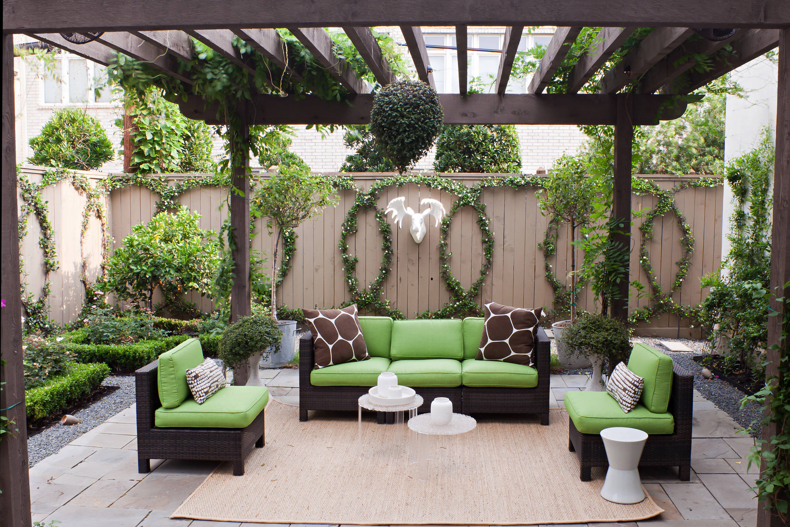 Stylish outdoor seating area with green cushions, wicker furniture, and decorative plants in a cozy garden space.